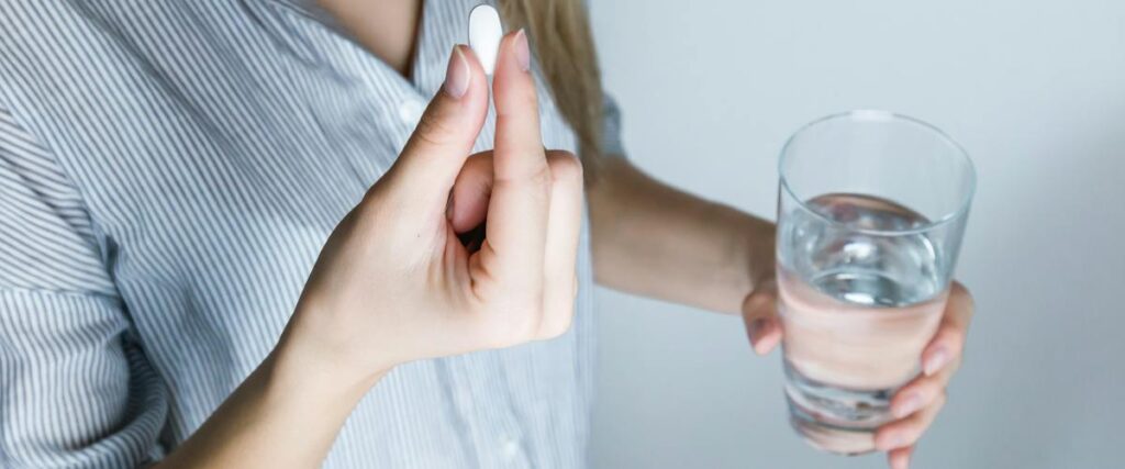 Woman holds a glass of water and medicine tablet