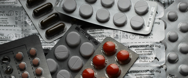 Assorted pharmaceutical tablets, capsules, and injectable vials arranged on a white surface